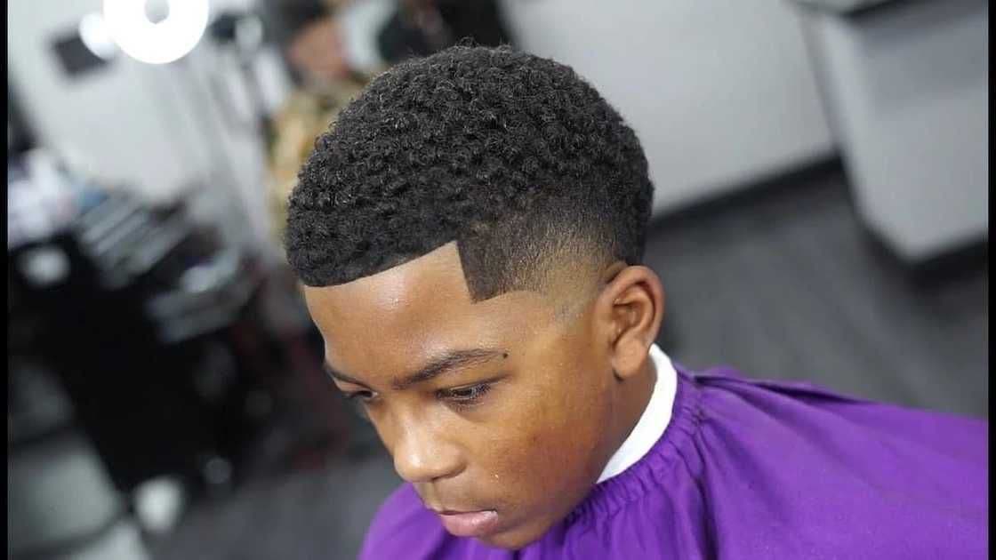 Young man with a fresh fade haircut, sharp line-up, and short curly hair on top.