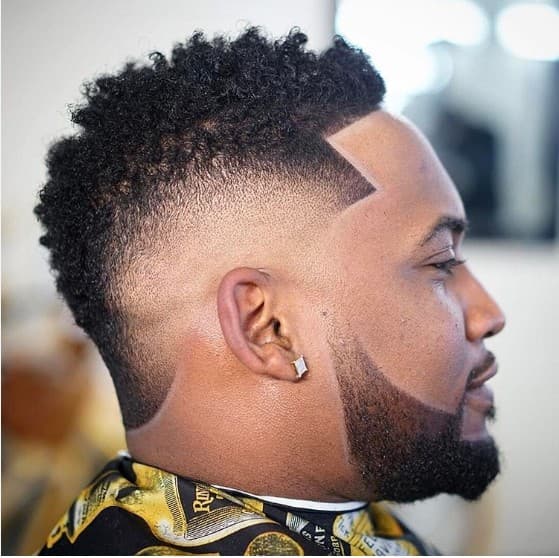 Side profile of a man with a curly high top fade and sharp beard lineup.