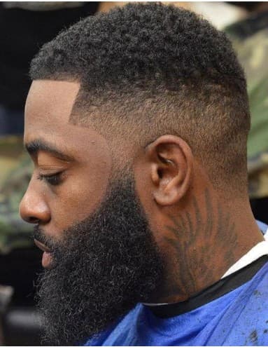 Man with a sharp skin fade, textured top, and a thick, well-groomed black beard.