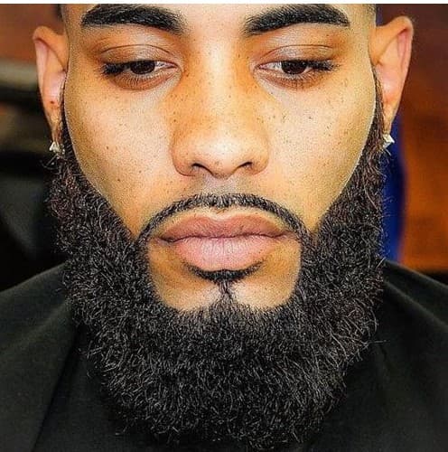 Close-up of a man with freckles, groomed eyebrows, and a thick, neatly shaped dark beard.
