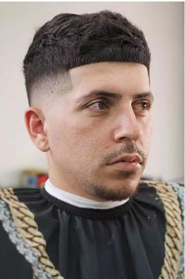 Man with a textured Caesar haircut, high skin fade, straight fringe, and a goatee.