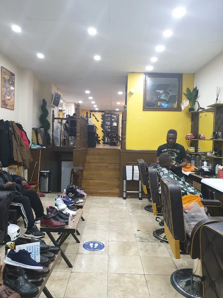 Barber cutting hair in a shop with yellow walls, barber chairs, and shoes on benches.