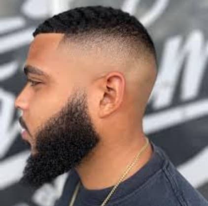 Side profile of a man with a sharp high skin fade and groomed full beard.
