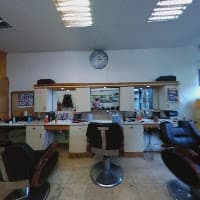 Barbershop interior featuring black leather chairs, mirrors, and a wall clock above the workstations.