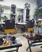 Barbershop interior featuring black and yellow chairs, mirrors, and shoes displayed on foreground tables.